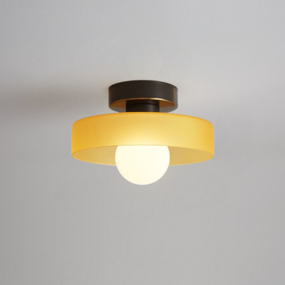 Ceiling light with a yellow glass disc shade on a black base, a frosted globe glowing beneath it