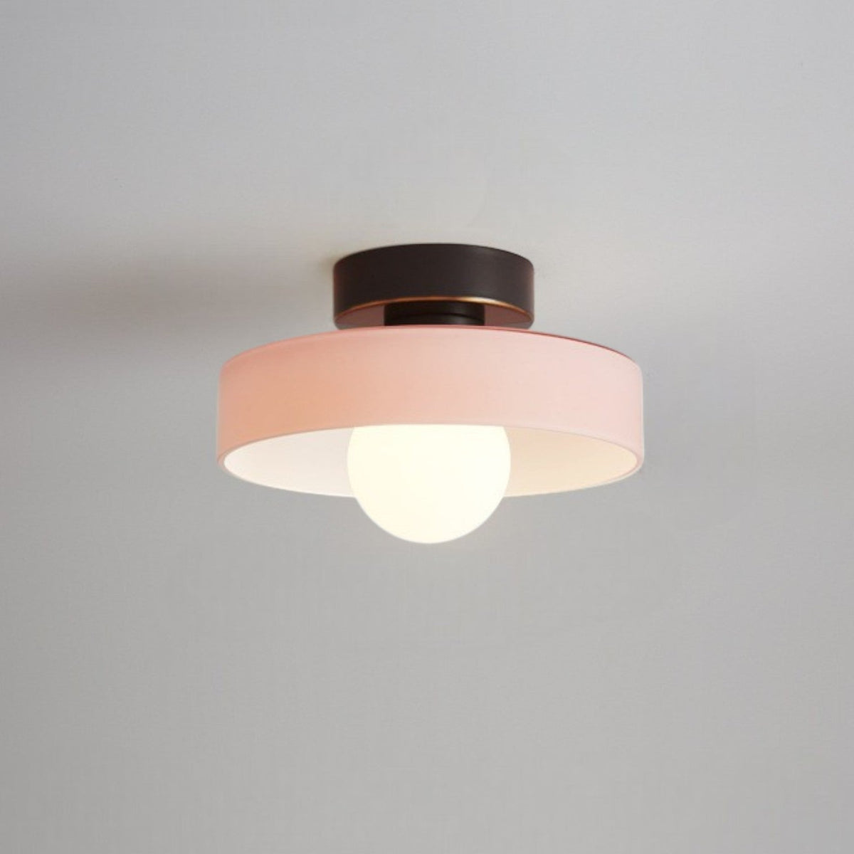 Ceiling light with a soft pink glass disc shade on a black base, a frosted globe glowing beneath it