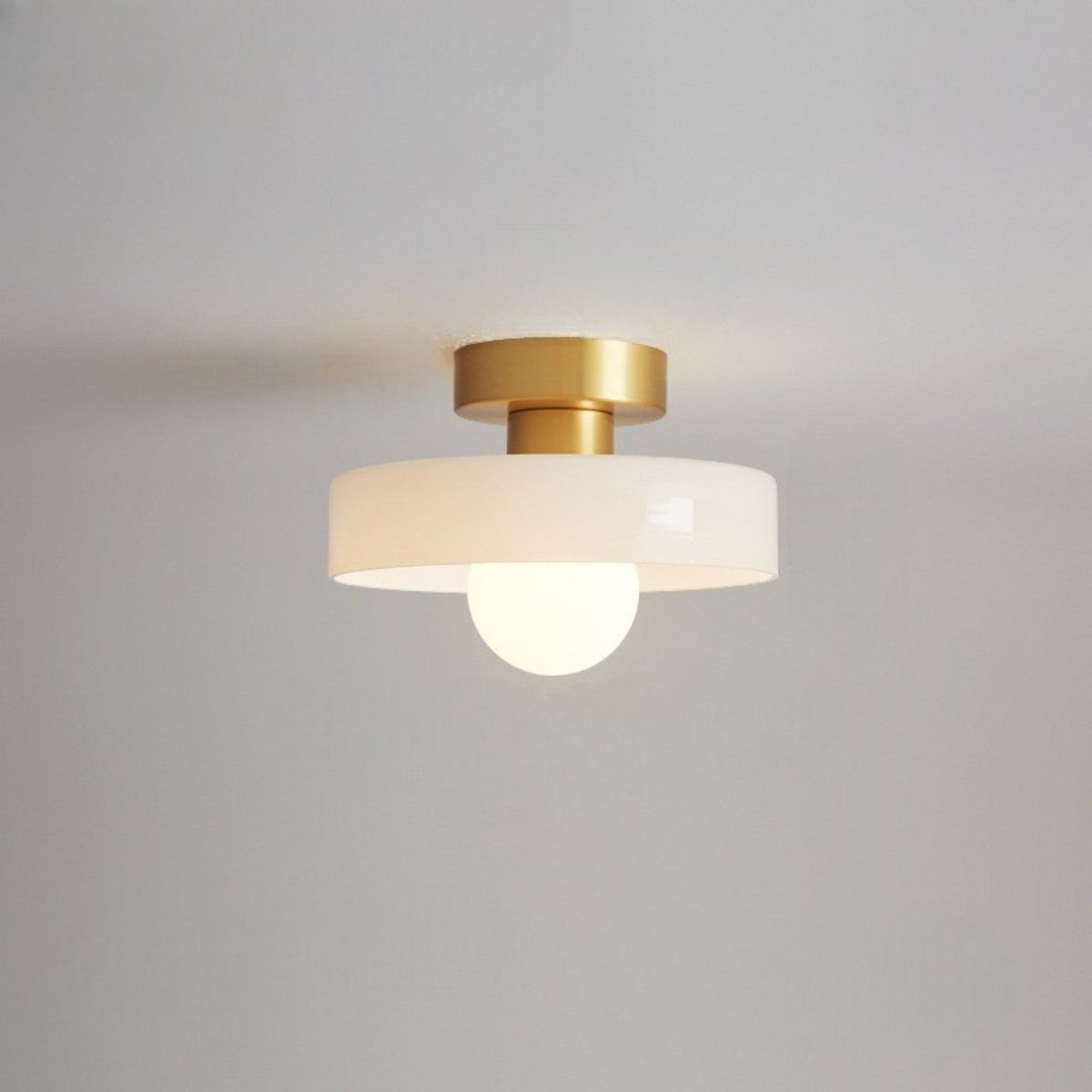 Ceiling light with a white glass disc shade on a gold-toned base, a frosted globe glowing beneath it