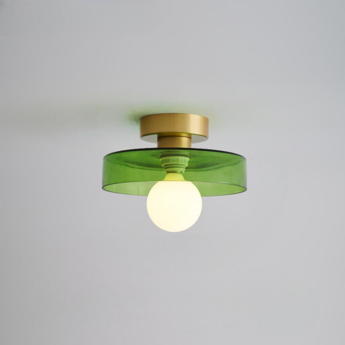 Ceiling light with a tinted green glass disc shade on a gold-toned base, lit from below by a frosted globe
