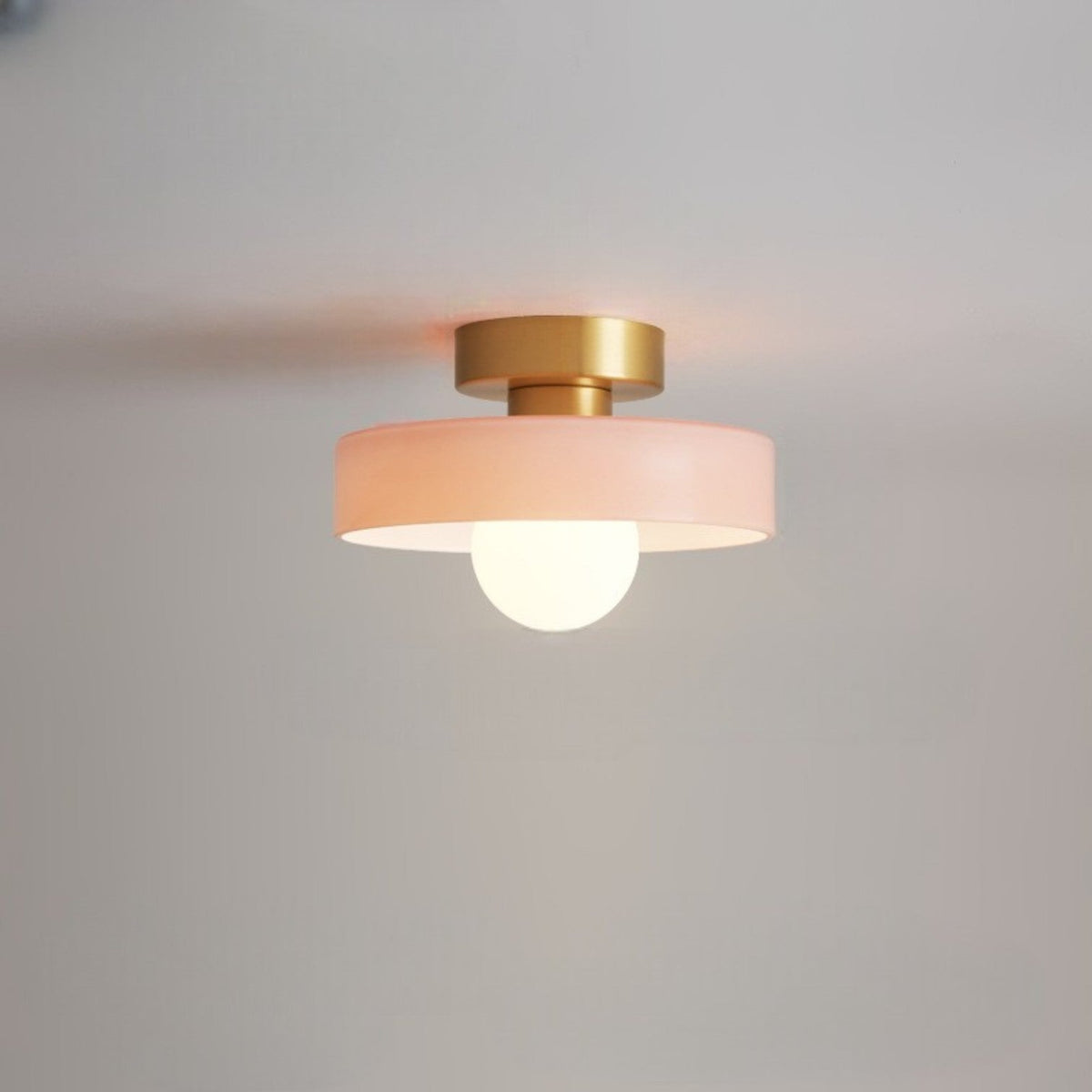 Ceiling light with a soft pink glass disc shade on a gold-toned base, a frosted globe glowing beneath it