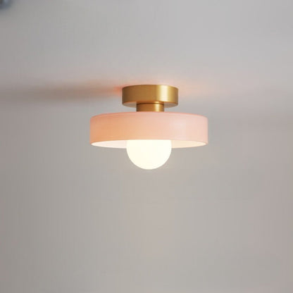Ceiling light with a soft pink glass disc shade on a gold-toned base, a frosted globe glowing beneath it