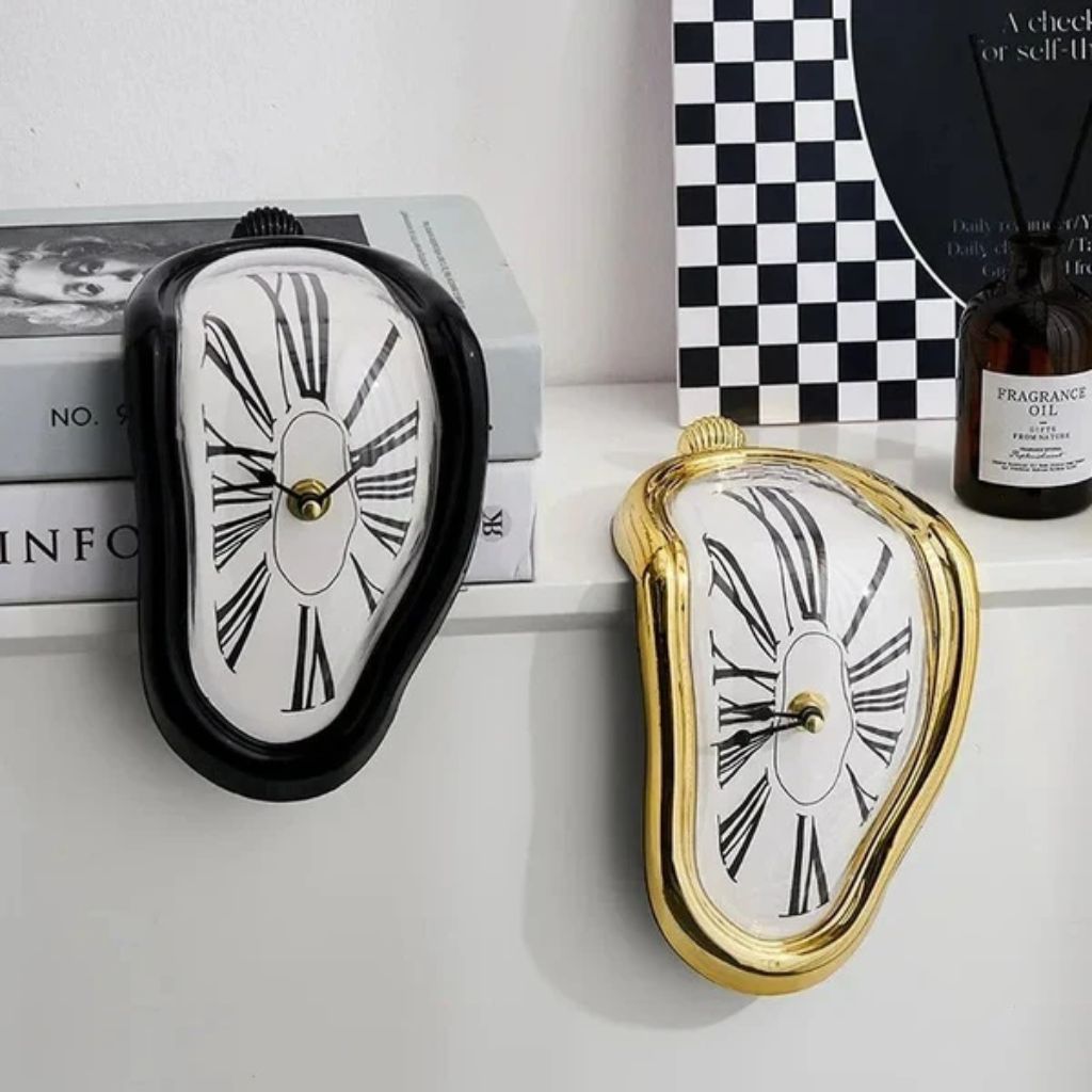 A black melting clock and a gold melting clock draped over the edge of a white shelf beside a stack of books