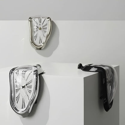 Three melting clocks in silver and black, two draped over the edge of a white block and one on the wall above