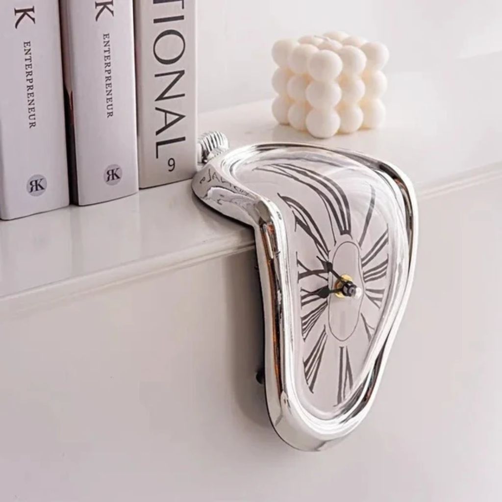 A silver melting clock draped over the edge of a white shelf beside a row of books