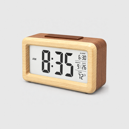 Wooden alarm clock in brown with a pale wood front frame and a lit screen showing time, alarm, date and temperature, on a light gray background