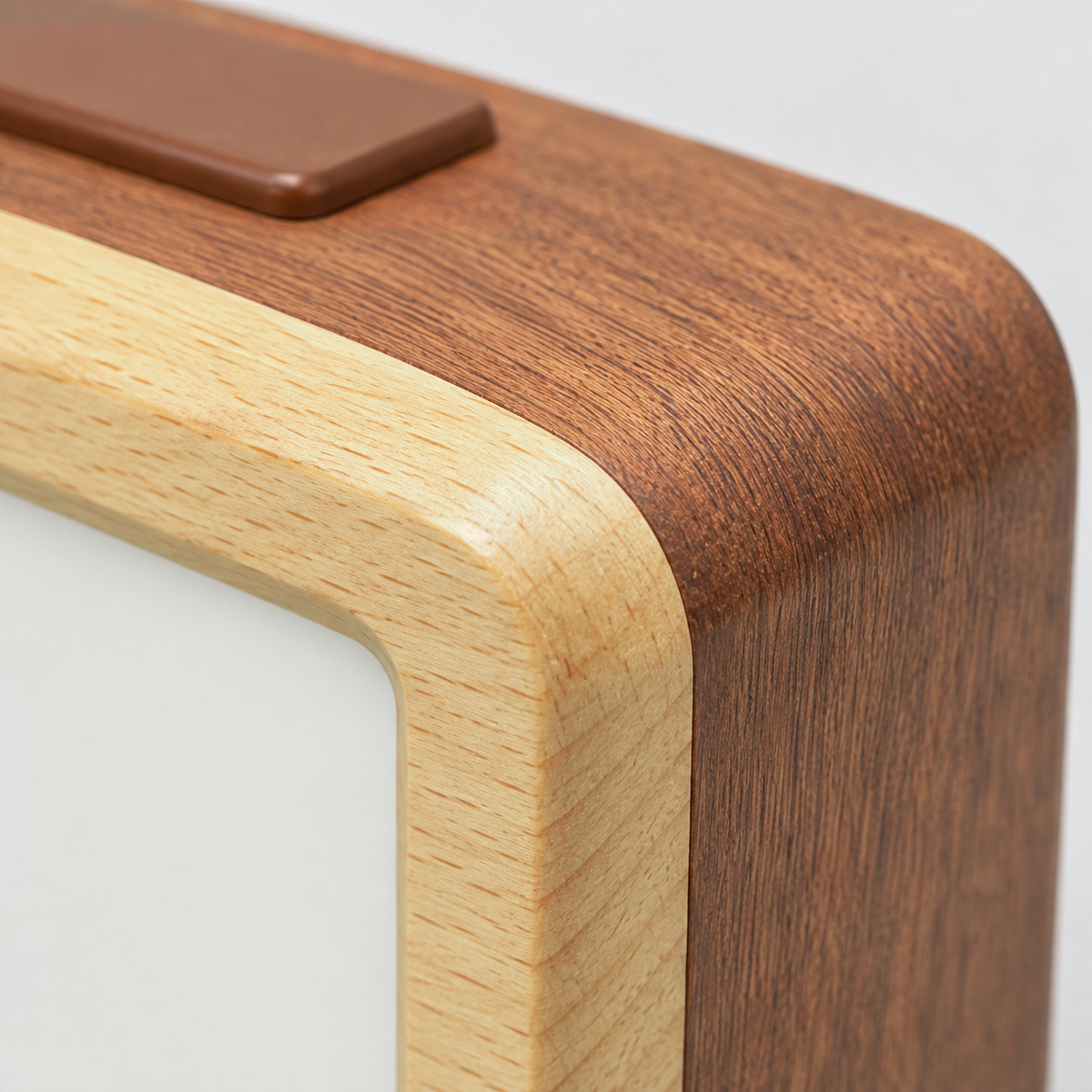 Close-up of the brown alarm clock's corner, where the pale wood front frame meets the reddish-brown wood body