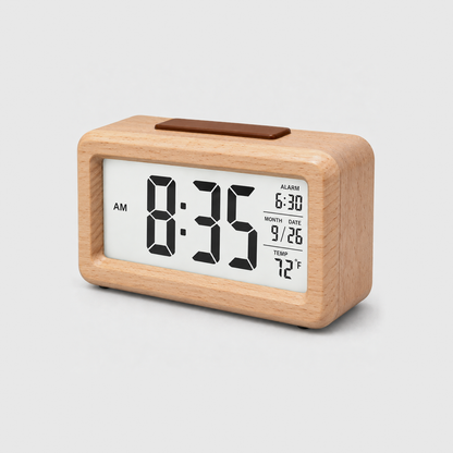 Wooden alarm clock in beige, pale wood all over, with a lit screen showing time, alarm, date and temperature, on a light gray background