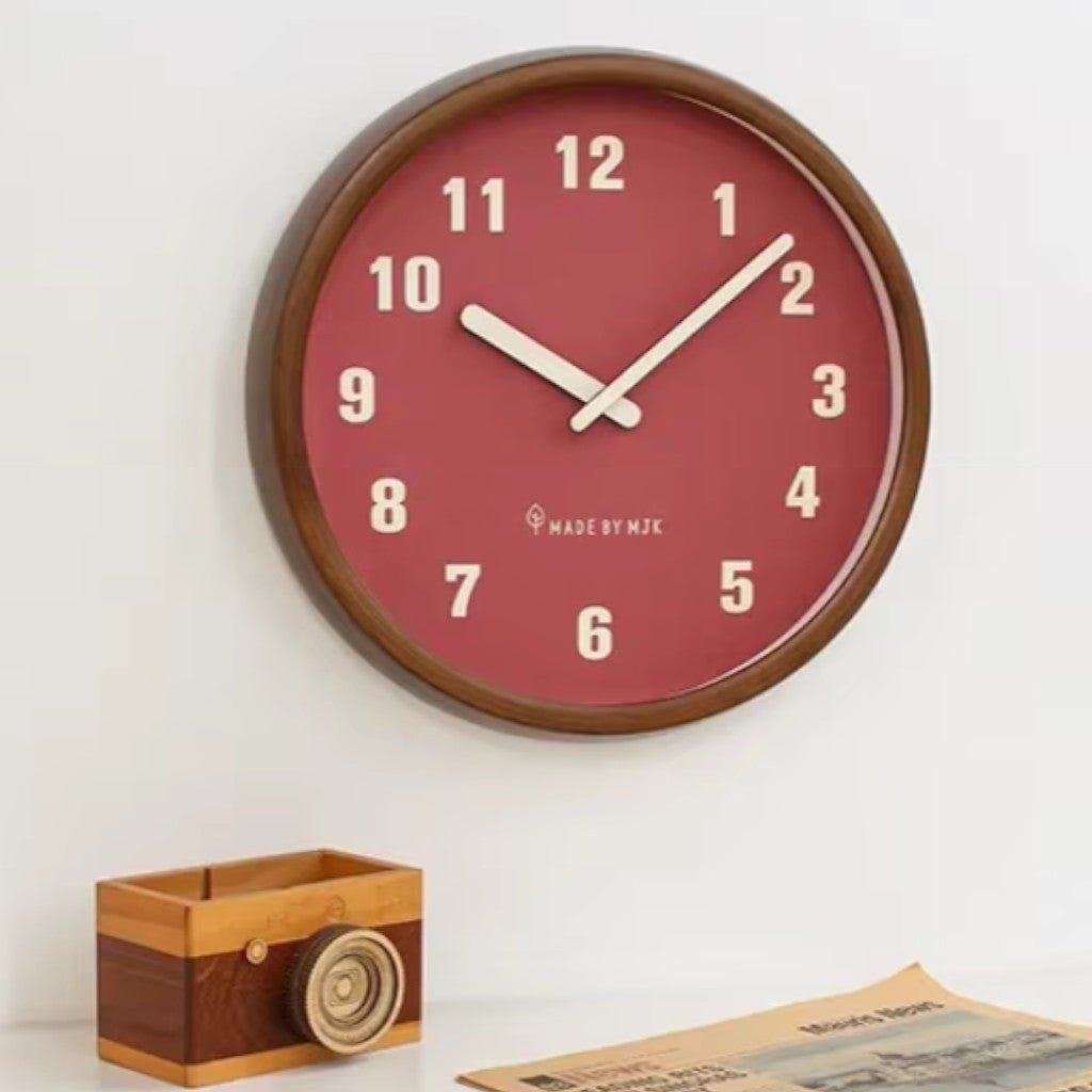 The Red wall clock with cream numbers and cream hands on a white wall above a small wooden desk tidy and a newspaper