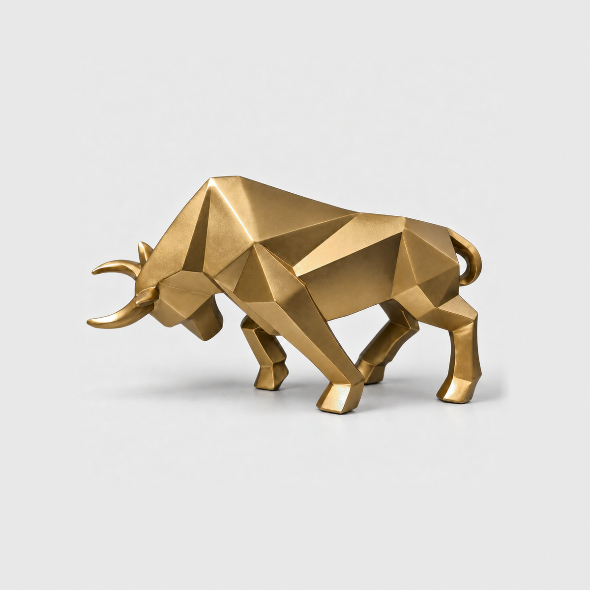 A gold geometric bull sculpture with faceted planes and forward-curving horns, standing on a light gray background