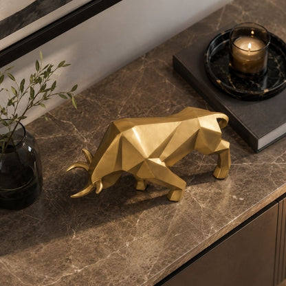 A gold geometric bull sculpture on a marble sideboard between a vase of greenery and a candle on a tray