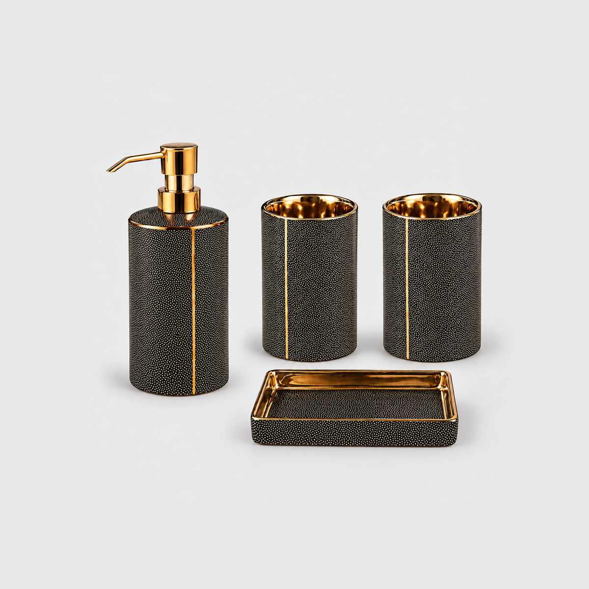 Black ceramic bathroom set of four with gold-coated trim: a soap dispenser with a gold-tone pump, two tumblers and a soap dish, on a plain light gray background