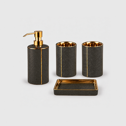 Black ceramic bathroom set of four with gold-coated trim: a soap dispenser with a gold-tone pump, two tumblers and a soap dish, on a plain light gray background