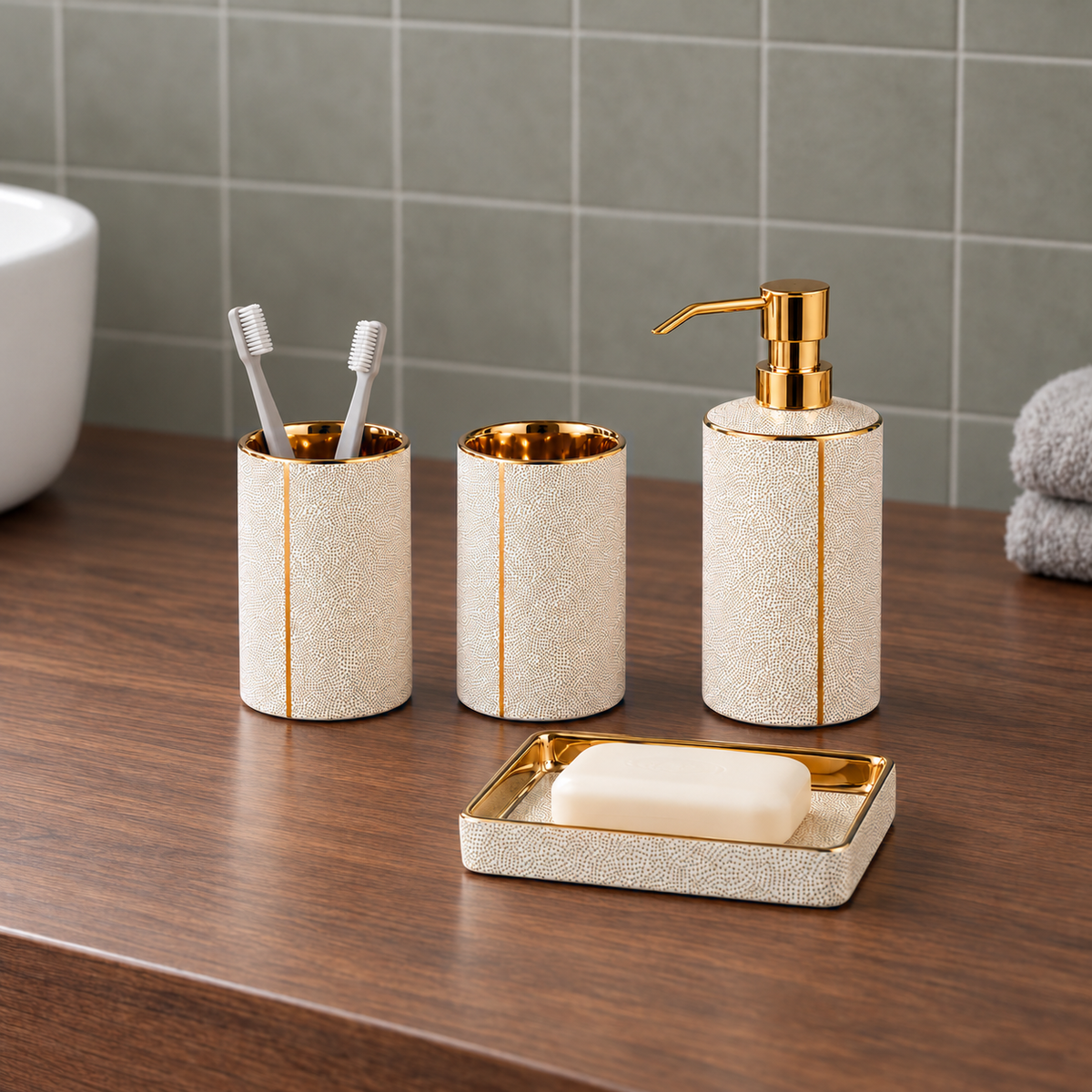 White ceramic soap dispenser, two tumblers and soap dish on a walnut vanity against sage gray tile in daylight