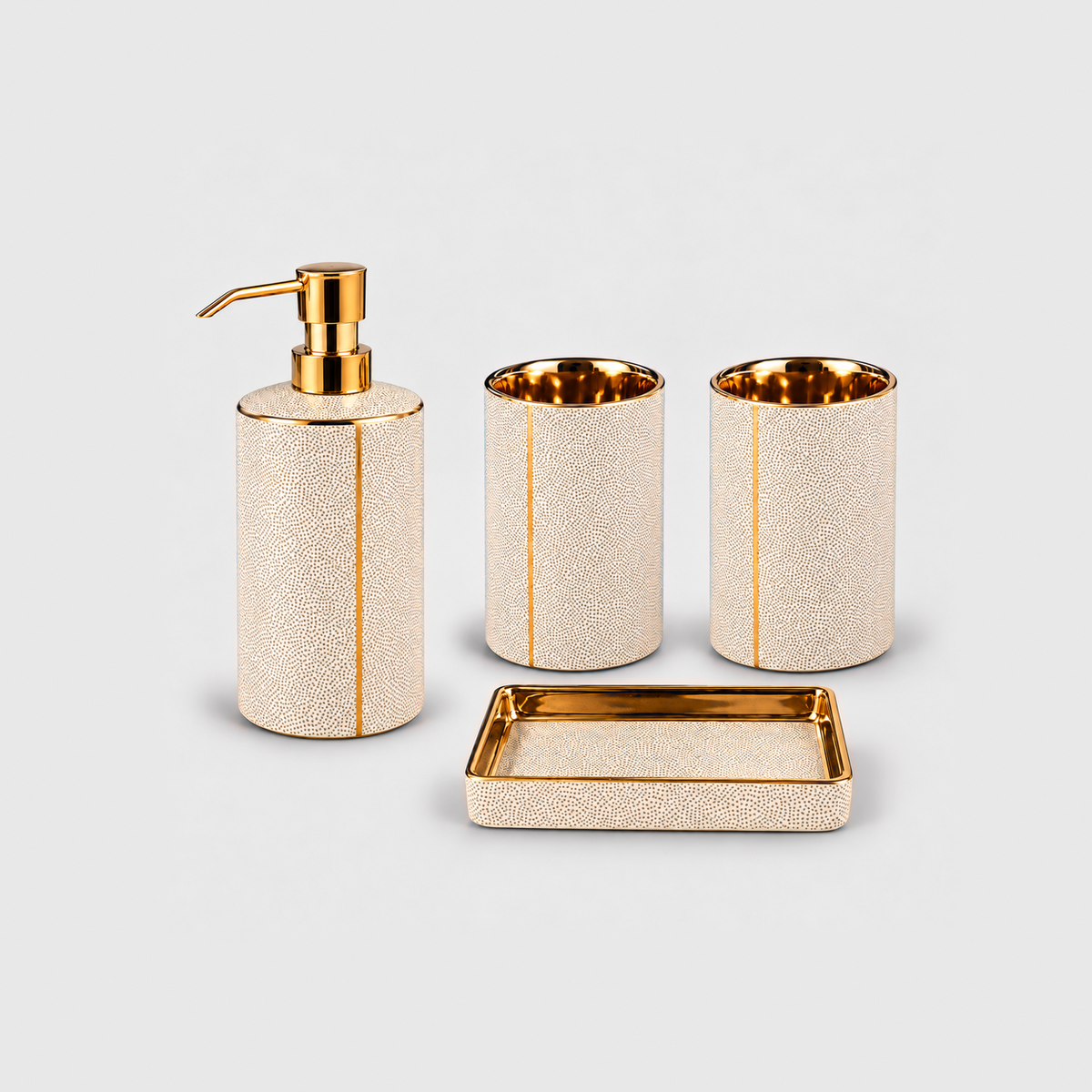 White ceramic bathroom set of four with gold-coated trim: a soap dispenser with a gold-tone pump, two tumblers and a soap dish, on a plain light gray background