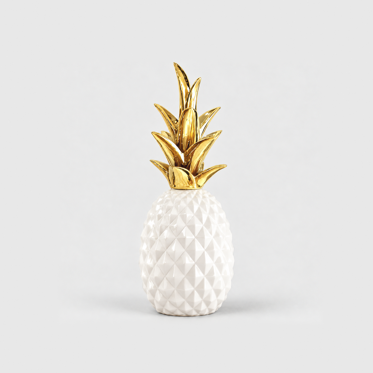A white resin pineapple sculpture with a glossy faceted body and a gold crown, standing on a light gray background