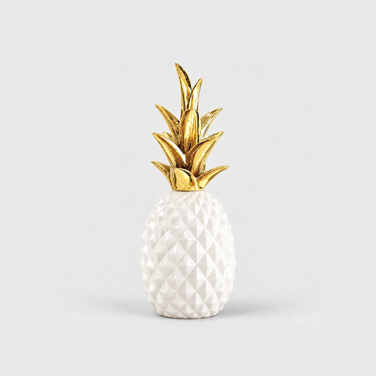 A white resin pineapple sculpture with a glossy faceted body and a gold crown, standing on a light gray background