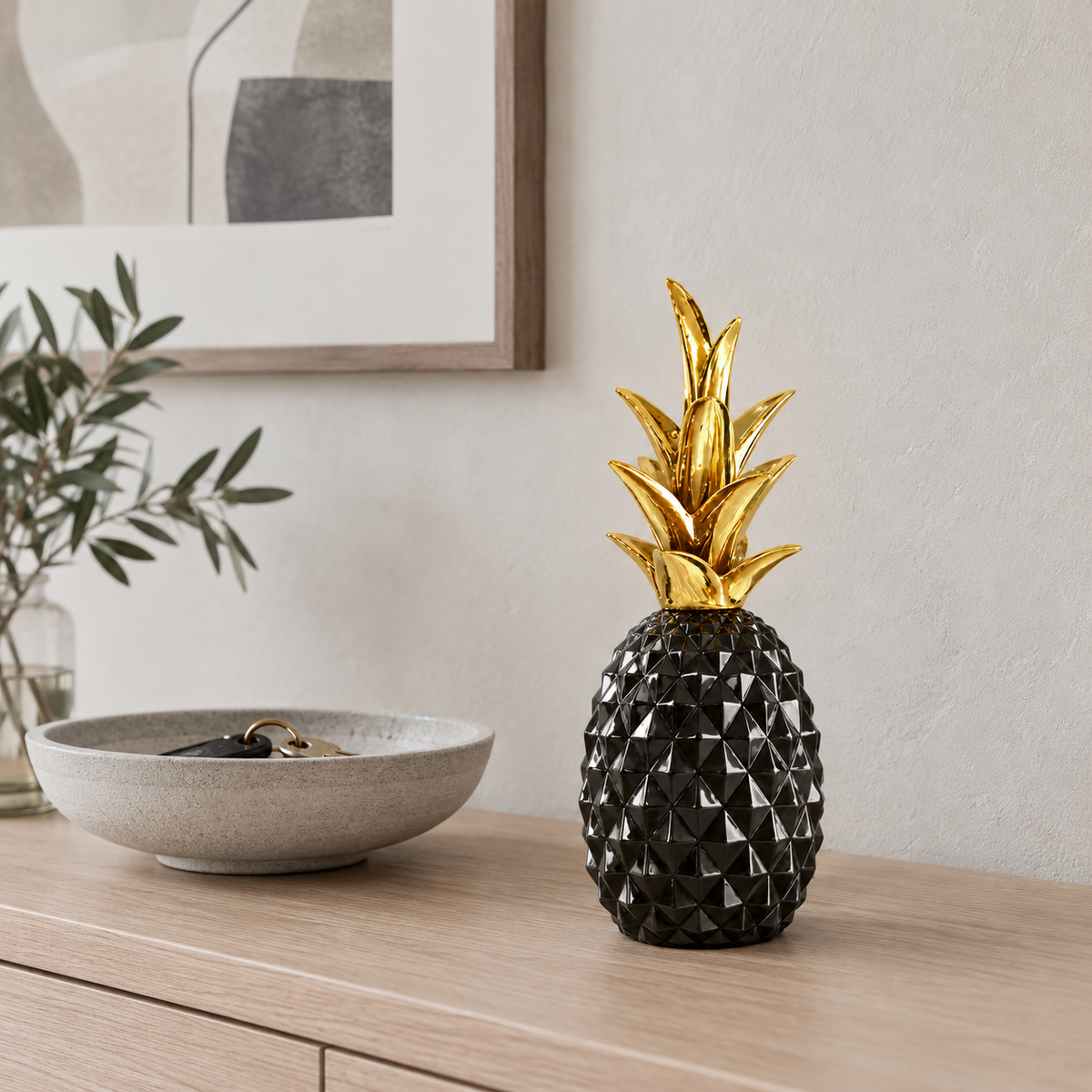 A glossy black faceted pineapple sculpture with a gold crown on a pale oak console table in an entrance hall