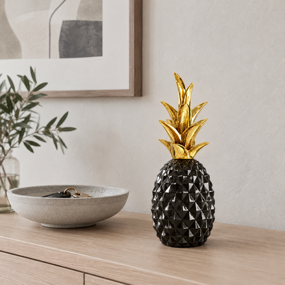 A glossy black faceted pineapple sculpture with a gold crown on a pale oak console table in an entrance hall