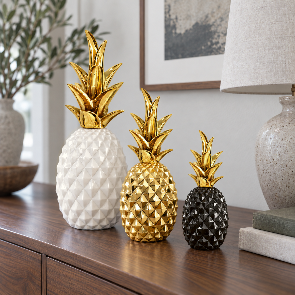 White, gold and black faceted pineapple sculptures in three sizes grouped on a walnut sideboard