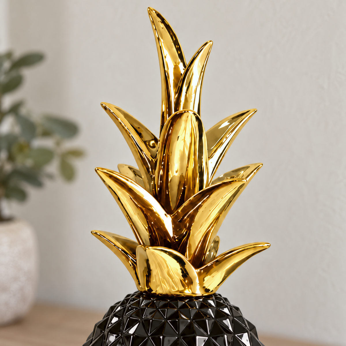 Close view of the mirror-gold crown of leaves rising from the glossy black pineapple sculpture