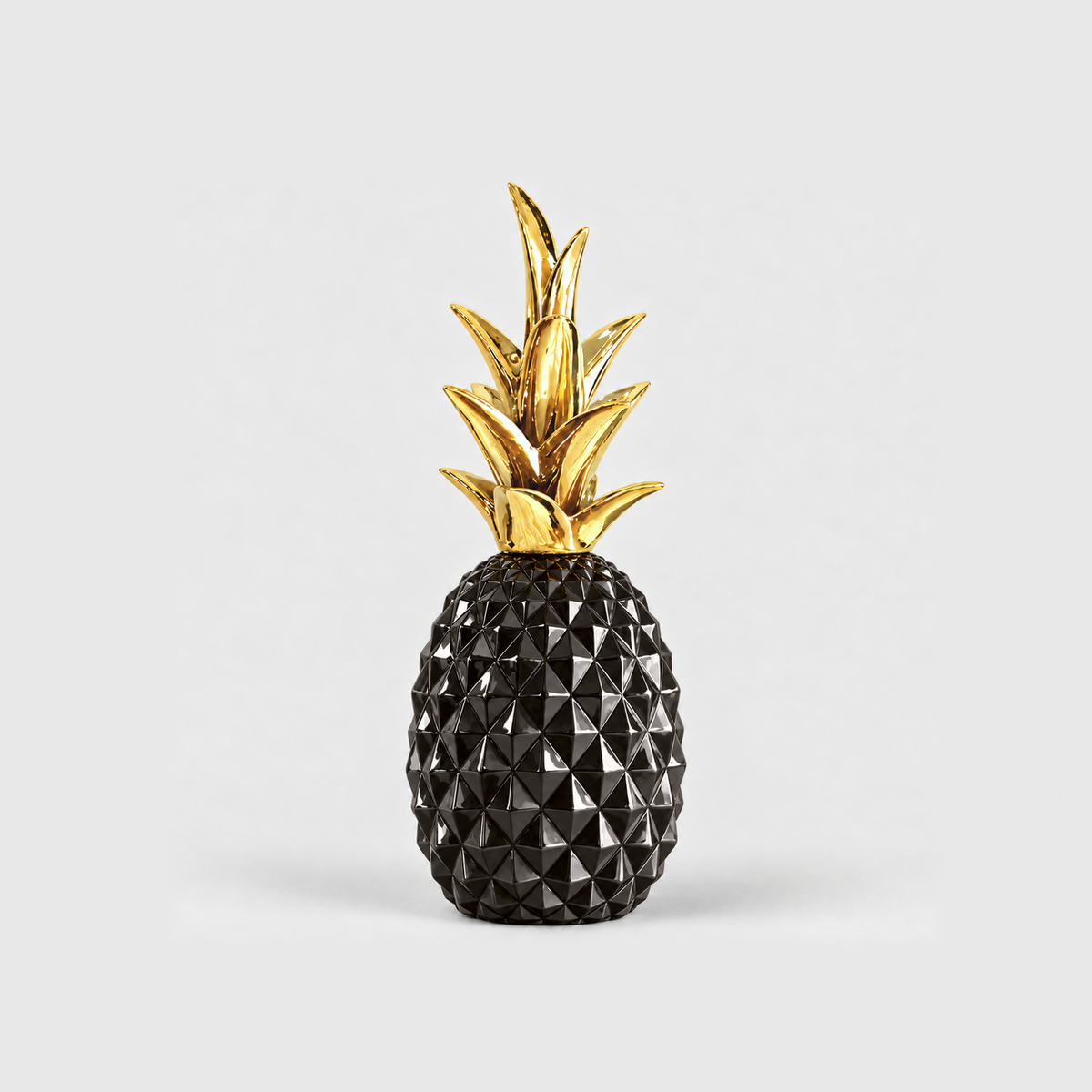 A glossy black resin pineapple sculpture with a faceted body and a gold crown, standing on a light gray background