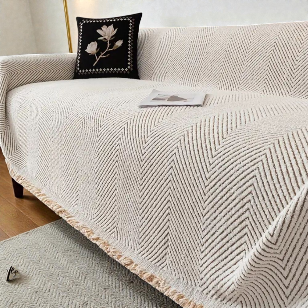 Ivory herringbone sofa cover draped over a sofa, taupe V-shaped lines in a soft pile with a natural fringe at the hem