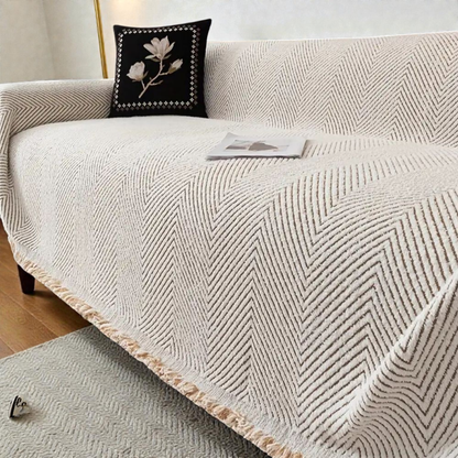 Ivory herringbone sofa cover draped over a sofa, taupe V-shaped lines in a soft pile with a natural fringe at the hem