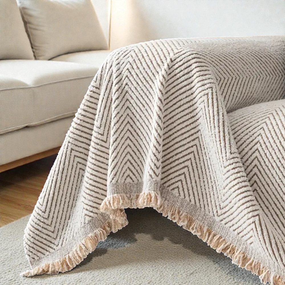 Ivory herringbone cover hanging loose over a sofa arm and seat, its fringed corner falling free above a gray rug