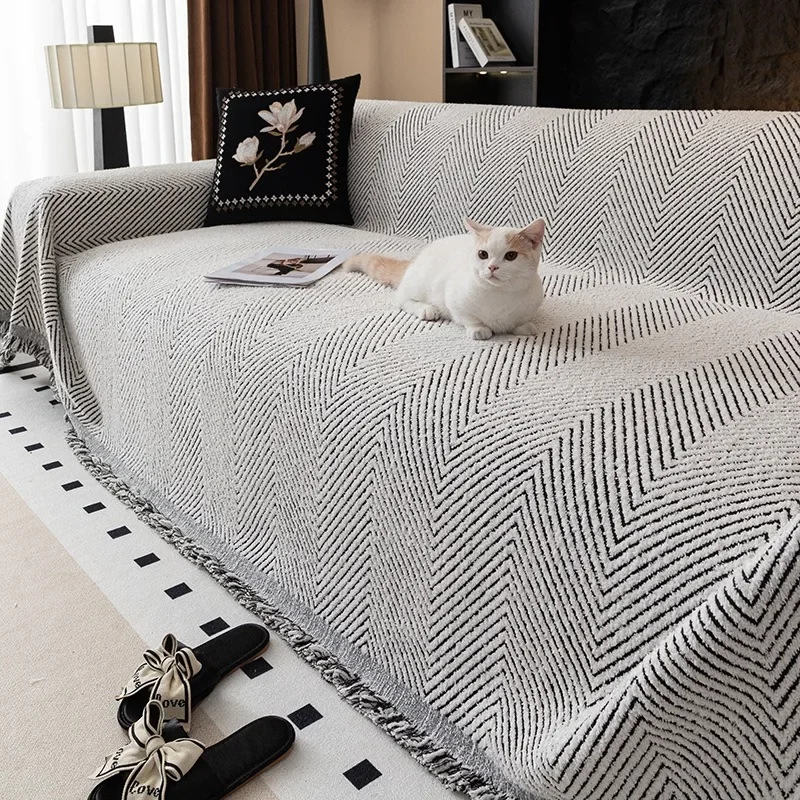 White cat lying on a gray herringbone sofa cover with black lines and a black and white fringe