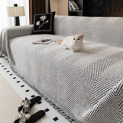 White cat lying on a gray herringbone sofa cover with black lines and a black and white fringe