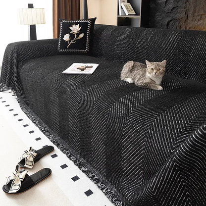 Tabby cat resting on a black herringbone sofa cover with fine white lines draped over a sofa