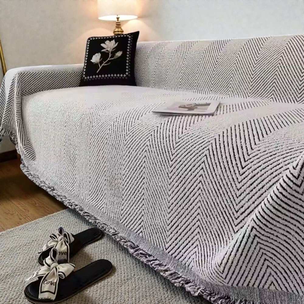 Gray herringbone sofa cover, a white ground with black lines, draped over a sofa with a black and white fringe