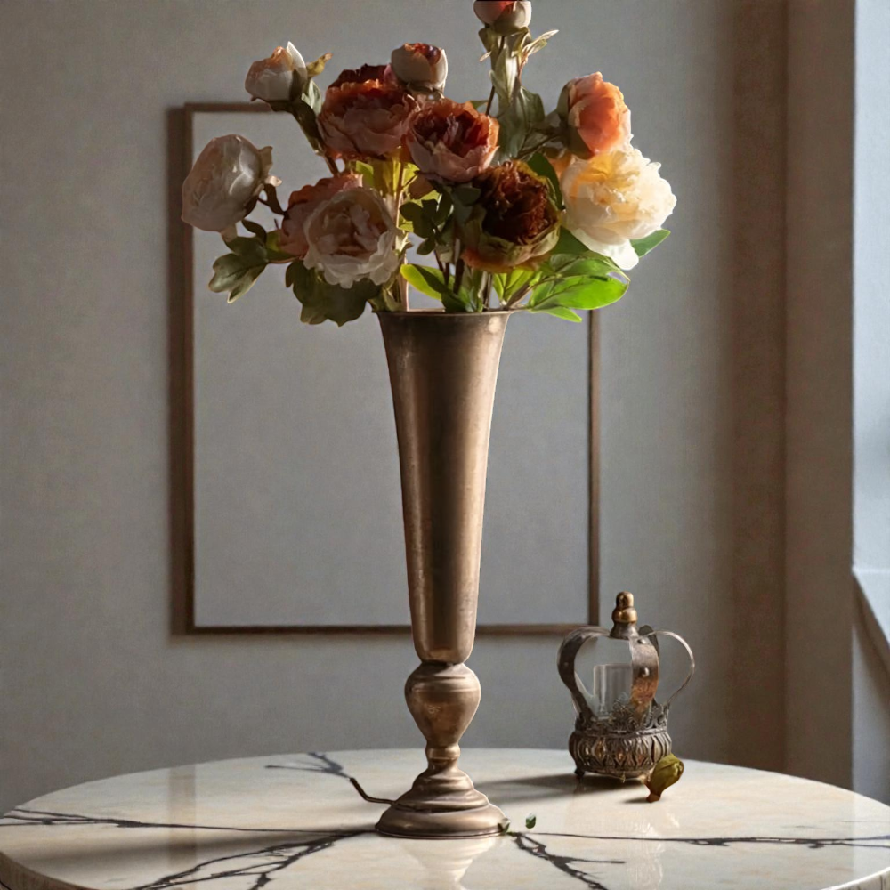 Tall antique gold trumpet vase holding orange and cream roses on a round marble table