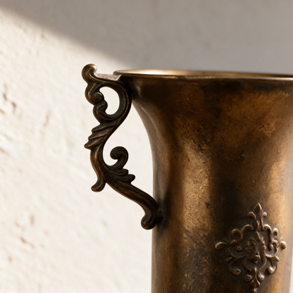 Close-up of the scrolled handle and raised crest on the antique gold urn vase
