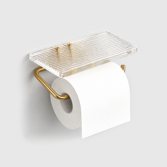 Toilet paper holder with a clear fluted acrylic shelf and a satin gold arm holding a white roll, fixed to a light gray wall