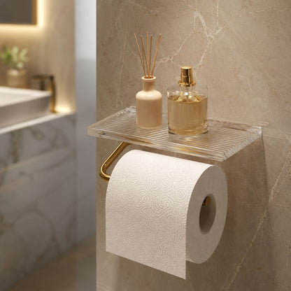 Gold toilet paper holder with a clear fluted shelf on a marble bathroom wall, a basin softly out of focus behind