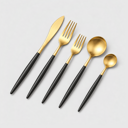 Gold flatware place setting with black handles: knife, fork, spoon, teaspoon and cake fork on a light gray background