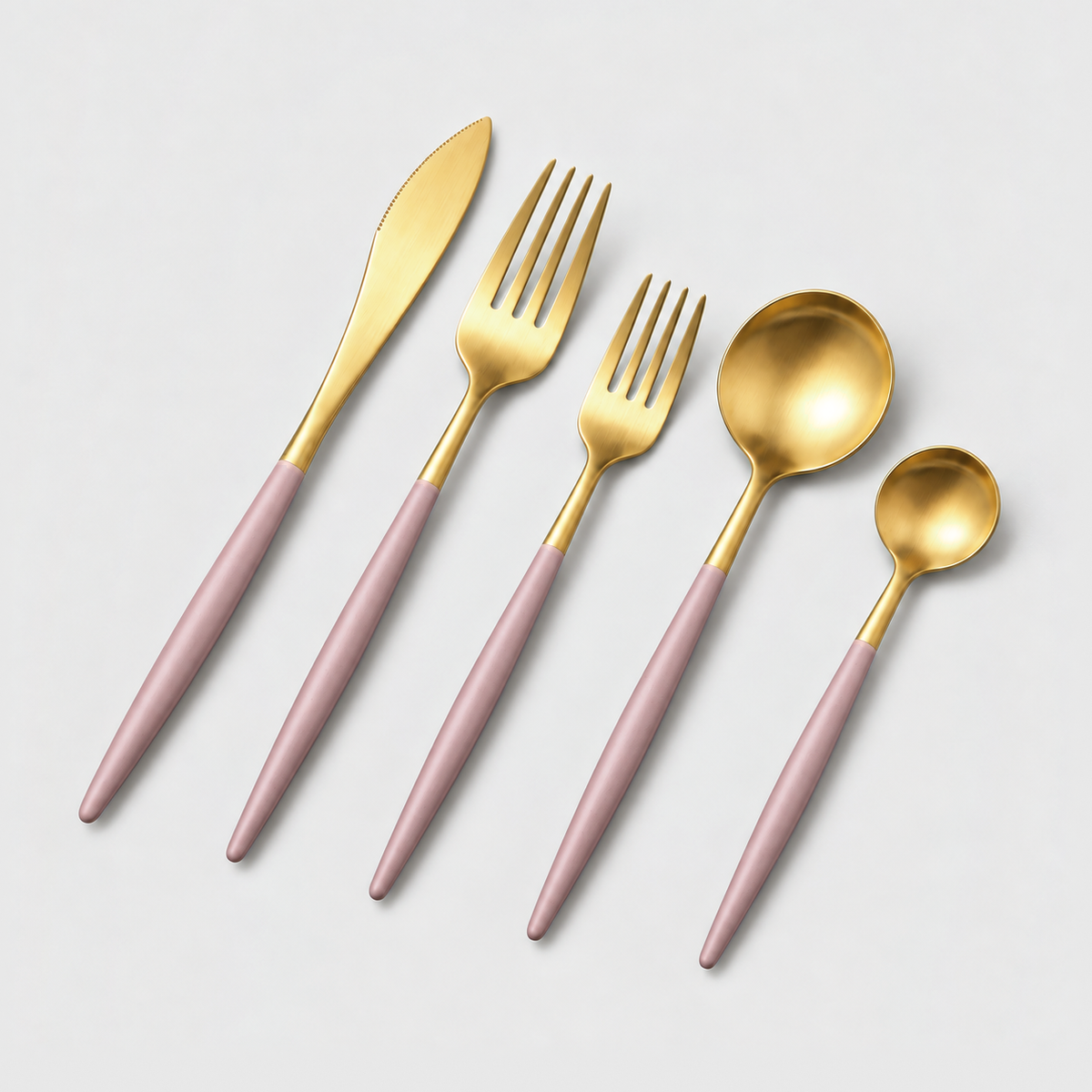 Gold flatware place setting with pink handles on a light gray background