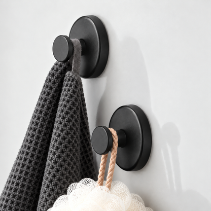 Two black suction hooks seen from the side, a charcoal waffle cloth on the upper one and a white loofah on its cord on the lower one