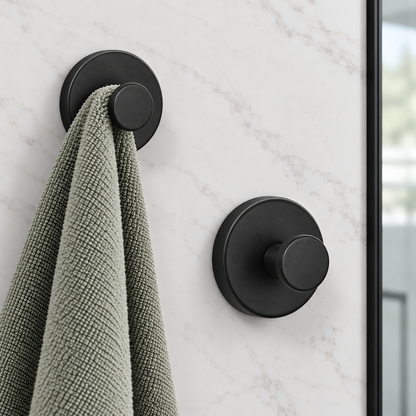 Black suction hooks on a marble shower wall, a sage towel on one and the other bare