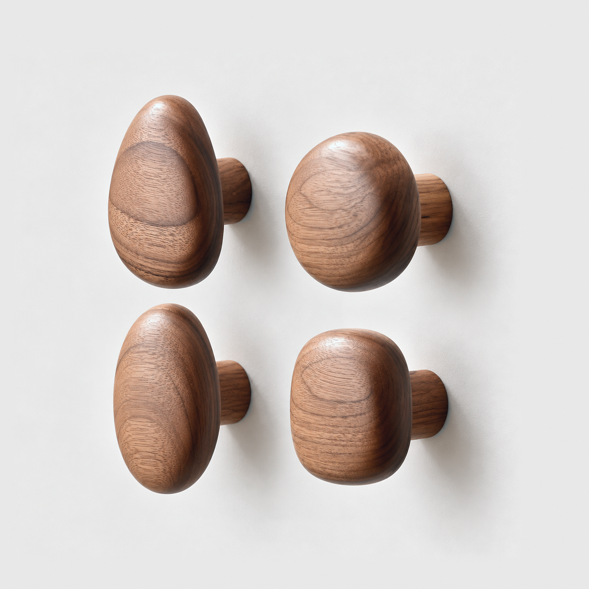 Set of four walnut pebble wall hooks in teardrop, round, oval and rounded square shapes on a plain gray wall