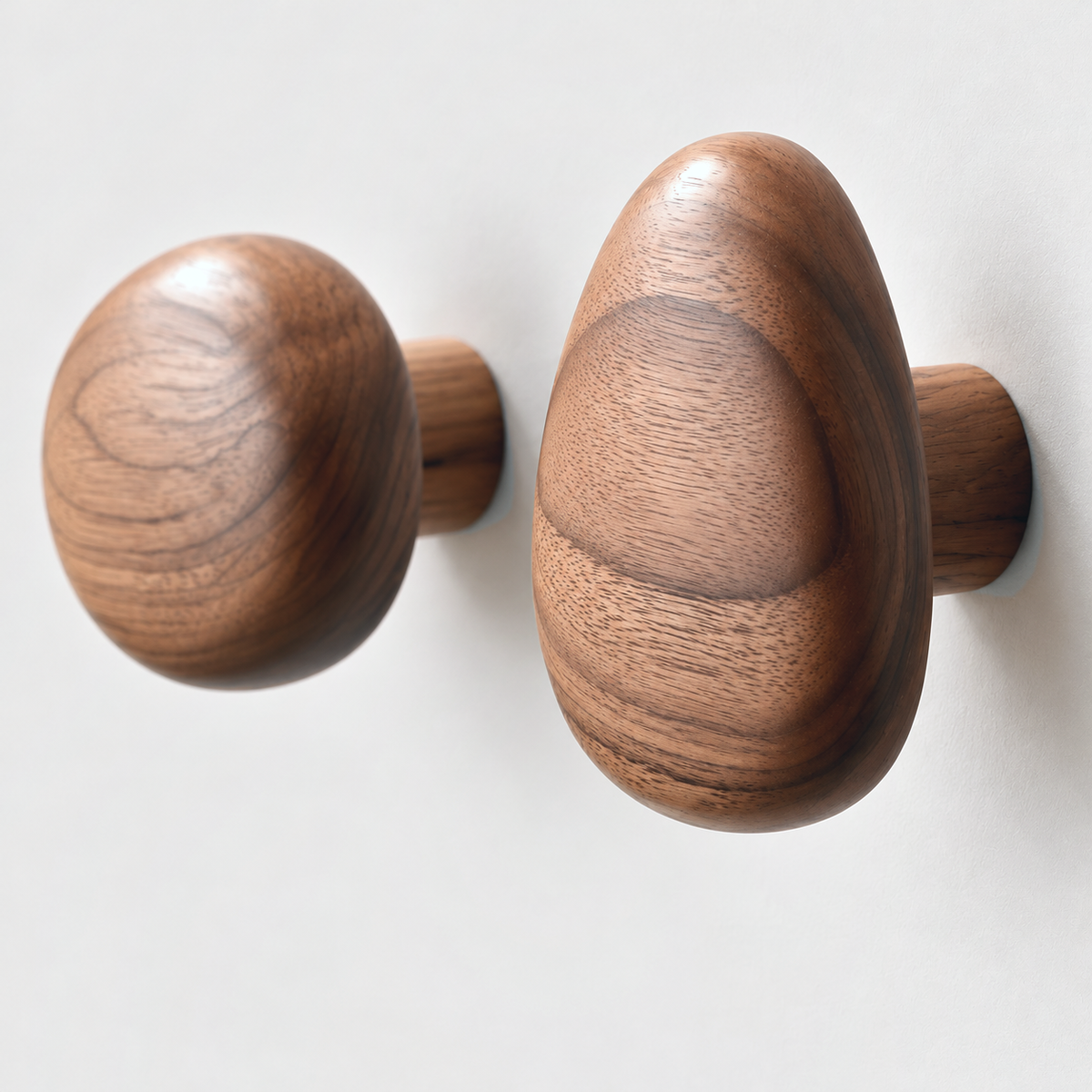 Close-up of walnut grain on teardrop and round pebble wall hooks showing the post and the gap to the wall