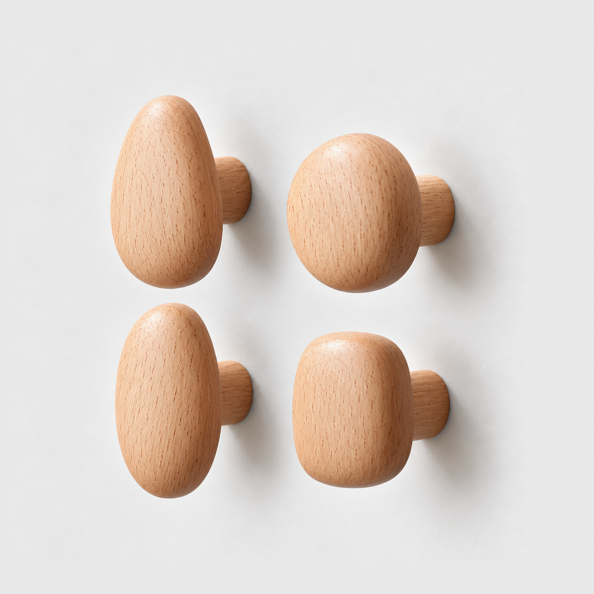 Set of four beech pebble wall hooks in teardrop, round, oval and rounded square shapes on a plain gray wall