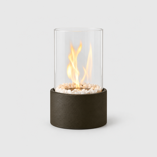 Black glass cylinder tabletop fire pit with a lit flame inside the clear glass and a matte textured base, on a light gray background