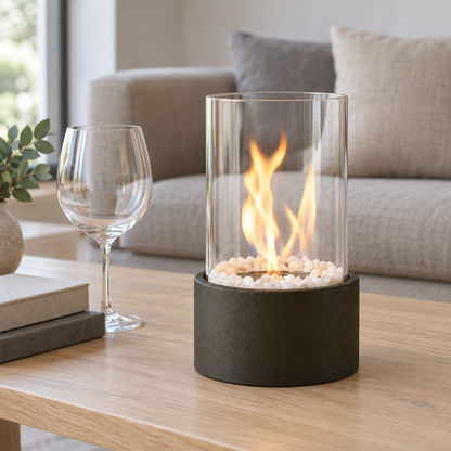 Black tabletop fire pit with a real flame on a pale oak coffee table in a daylit living room beside a wine glass and books