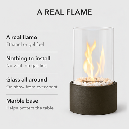 Black glass cylinder fire pit with text: a real flame on ethanol or gel fuel, nothing to install, glass all around, a marble base that helps protect the table