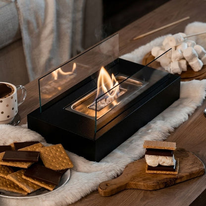 Lit tabletop fire pit on a fur runner on a coffee table, with marshmallows, crackers, chocolate and a mug around it