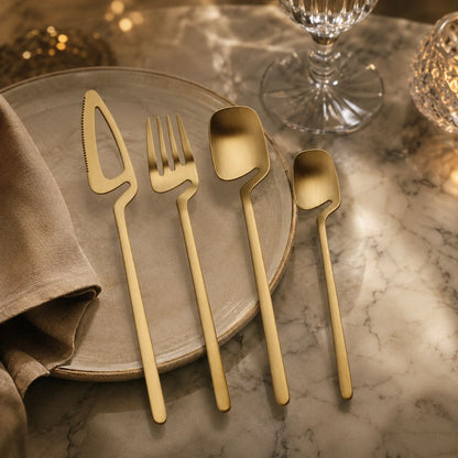 Gold flatware knife, fork, spoon and teaspoon on a stoneware plate on a marble table with a linen napkin