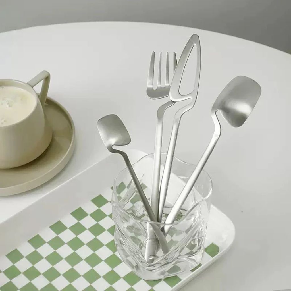 Silver flatware standing in a glass on a breakfast table beside a cup
